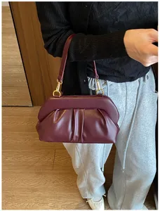 Borsa morbida bordeaux con pieghe, dettagli dorati e tracolla, mostrata indossata