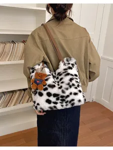 Rückansicht einer schwarz-weiß gefleckten Plüschtasche mit braunem Riemen und Teddybär-Anhänger