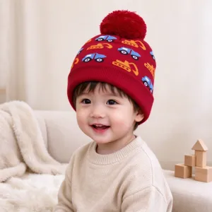 Child wearing a red knitted hat with colorful construction vehicle motifs, a folded brim and pompom
