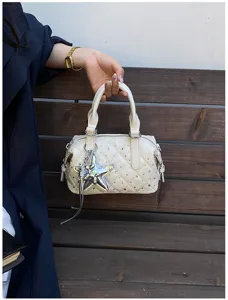 Dettaglio di borsa avorio trapuntata con strass e ciondolo a stella argentato, tenuta dai manici