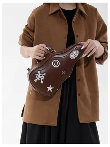 Borsa marrone a forma di chitarra con toppe ricamate, mostrata in mano su uno sfondo chiaro