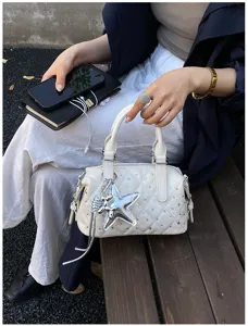 Borsa bianca trapuntata con strass e ciondolo a stella argentato, tenuta da una persona seduta