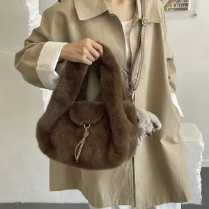 Brown fluffy faux-fur handbag with a detachable shoulder strap, shown carried with a beige coat