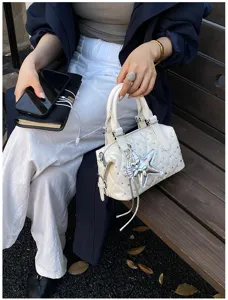 Borsa bianca trapuntata con strass e stella argentata, tenuta per i manici su una panchina