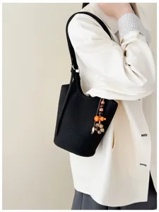 Detalle del bolso negro al hombro, con textura de cocodrilo, cuentas de madera y colgante naranja