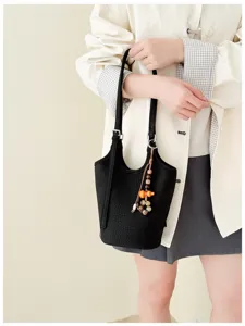 Una modelo sostiene un bolso negro texturizado con colgante de cuentas coloridas ante un fondo claro.