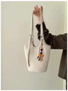 Bolso marfil con textura de cocodrilo, correa ajustable y colgante de cuentas, visible en detalle