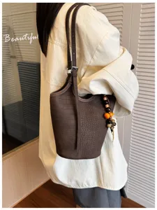 Bolso marrón con textura grabada al hombro, con correa ajustable y colgante de cuentas de madera