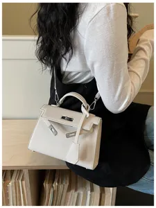Una donna porta una borsa color crema testurizzata, con patta, chiusura argentata e tracolla
