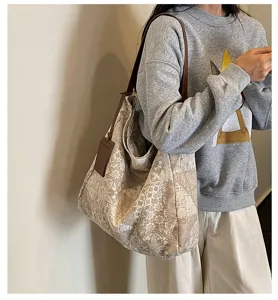 Borsa jacquard beige indossata da una modella, con tracolla in pelle marrone e ciondolo decorativo