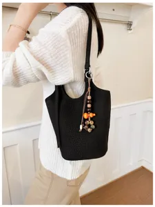 Bolso negro con relieve de cocodrilo, llevado al hombro con correa larga y colgante de cuentas
