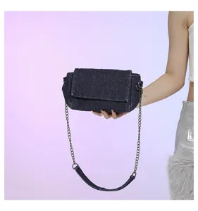 Borsa in denim blu scuro con impunture a rombi, patta e tracolla a catena metallica, tenuta in mano