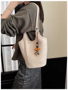 Modelo luce un bolso cubo color crema con relieve de cocodrilo, correa al hombro y colgante decorativo