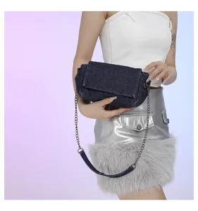 Modella mostra una borsa in denim scuro con patta, cuciture visibili e lunga catena argentata