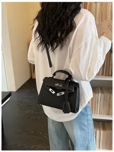 Vista da dietro di una modella con borsa nera strutturata a patta, chiusura argentata e tracolla