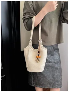 La modelo lleva un bolso bombonera crema con relieve de cocodrilo, tiras finas y colgante de cuentas