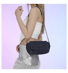Vista laterale di una modella con borsa in denim blu scuro con patta e tracolla a catena argentata
