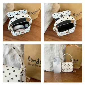 Open white mini bag with black polka dots, gold clasp and chain, shown with phone for scale