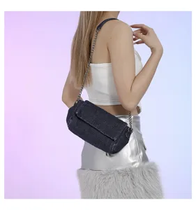 Modella con borsa in denim scuro con patta e catena argentata, su uno sfondo pastello tenue