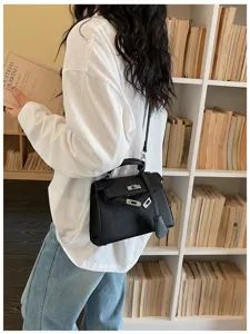 Borsa nera con grana e dettagli argentati indossata a tracolla davanti a una libreria chiara