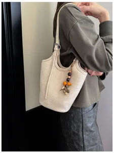 Vista de bolso marfil con textura de cocodrilo, llevado al hombro y con colgante de cuentas