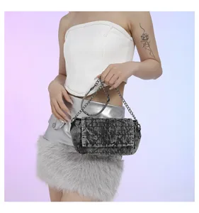 La modella tiene una borsa a patta in denim grigio slavato con catene argentate su sfondo pastello