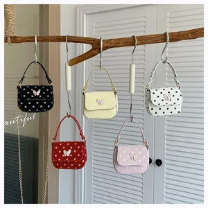 Five polka-dot mini bags with butterfly clasps hang from a branch in assorted colors