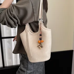 Bolso cubo color crema con textura de cocodrilo en relieve y colgante de cuentas, llevado al hombro