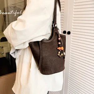 Bolso cubo marrón con textura de cocodrilo, correa al hombro y adorno de cuentas, llevado al hombro