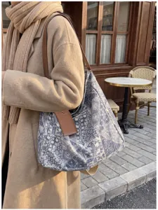 Borsa jacquard blu-grigia con tracolla in pelle marrone, indossata a spalla in un caffè