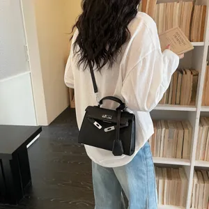 Borsa nera strutturata in similpelle, con chiusura metallica e ciondolo, portata a tracolla