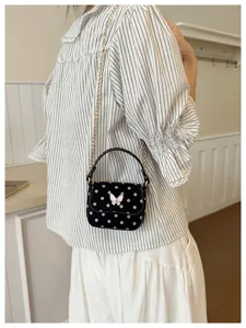 Le modèle porte un petit sac noir à pois blancs, avec un fermoir nœud et une chaîne dorée.