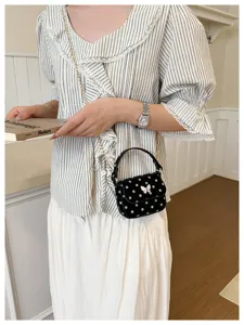 Petit sac noir à pois blancs avec fermoir papillon, porté à la taille par une chaîne dorée.