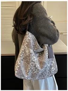 Borsa in tela grigia con motivi folk bianchi, indossata a spalla con cinghie in pelle marrone