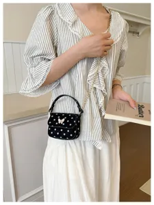 Sac noir à pois blancs, avec nœud rose et chaîne dorée, porté dans un intérieur lumineux