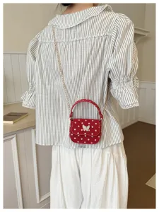 Vue de dos d’une tenue avec un petit sac rouge à pois blancs, nœud blanc et chaîne dorée