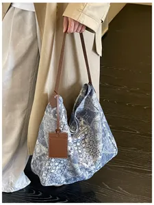 Borsa blu in tessuto floreale, con tracolle marroni e portacarte, accanto a un cappotto beige