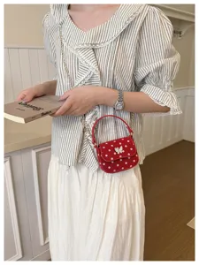 Une femme tient un livre près d'un petit sac rouge à pois, orné d'un fermoir papillon blanc