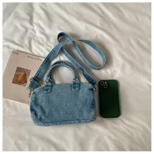 Sac en denim délavé bleu clair, anses arrondies et bandoulière réglable, posé près d’un téléphone