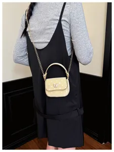 Détail d’un mini-sac jaune à pois blancs et motif nœud, porté avec une chaîne dorée