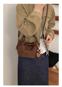 Sac seau marron à pois en velours porté à l'épaule, avec anses en cuir et breloque en bois