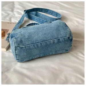 Gros plan sur les coutures du fond du sac en denim délavé, avec sa bandoulière sur tissu blanc