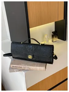 Zwarte tas met krokodillenreliëf en gouden sluiting, gestyled op boeken in een sfeervol interieur