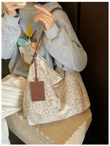 Borsa beige con motivi vintage bianchi e targhetta in pelle marrone, portata a spalla