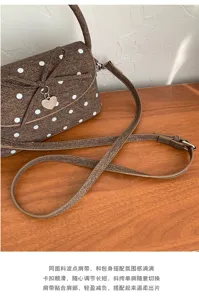 Dettaglio della borsa marrone a pois bianchi, con fiocco, ciondolo a cuore e tracolla regolabile