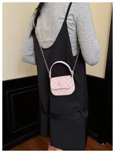 Porté par un modèle, petit sac rose à pois blancs, papillon doré, bandoulière chaîne et poignée