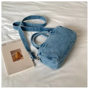 Vue plongeante d’un sac en denim délavé avec bandoulière et pièces métalliques sur un lit blanc
