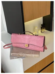 Roze tas met krokodillenstructuur en goudkleurige sluiting op kunstboeken naast parfumflesjes