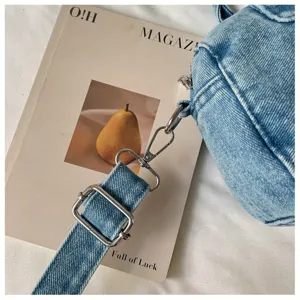 Gros plan sur une bandoulière en denim bleu clair délavé, avec boucle et mousqueton argentés