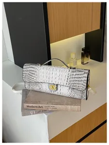 Witte tas met krokodillenstructuur en gouden sluiting, getoond op een boek in een modern interieur